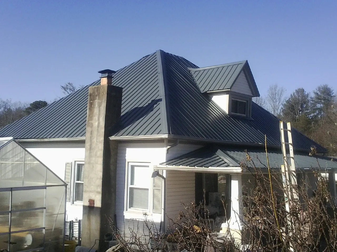 Dark blue standing seam metal roof on a white farmhouse with dormer — Slate & Tile Roof Repair by Roofing Brothers in Bronx