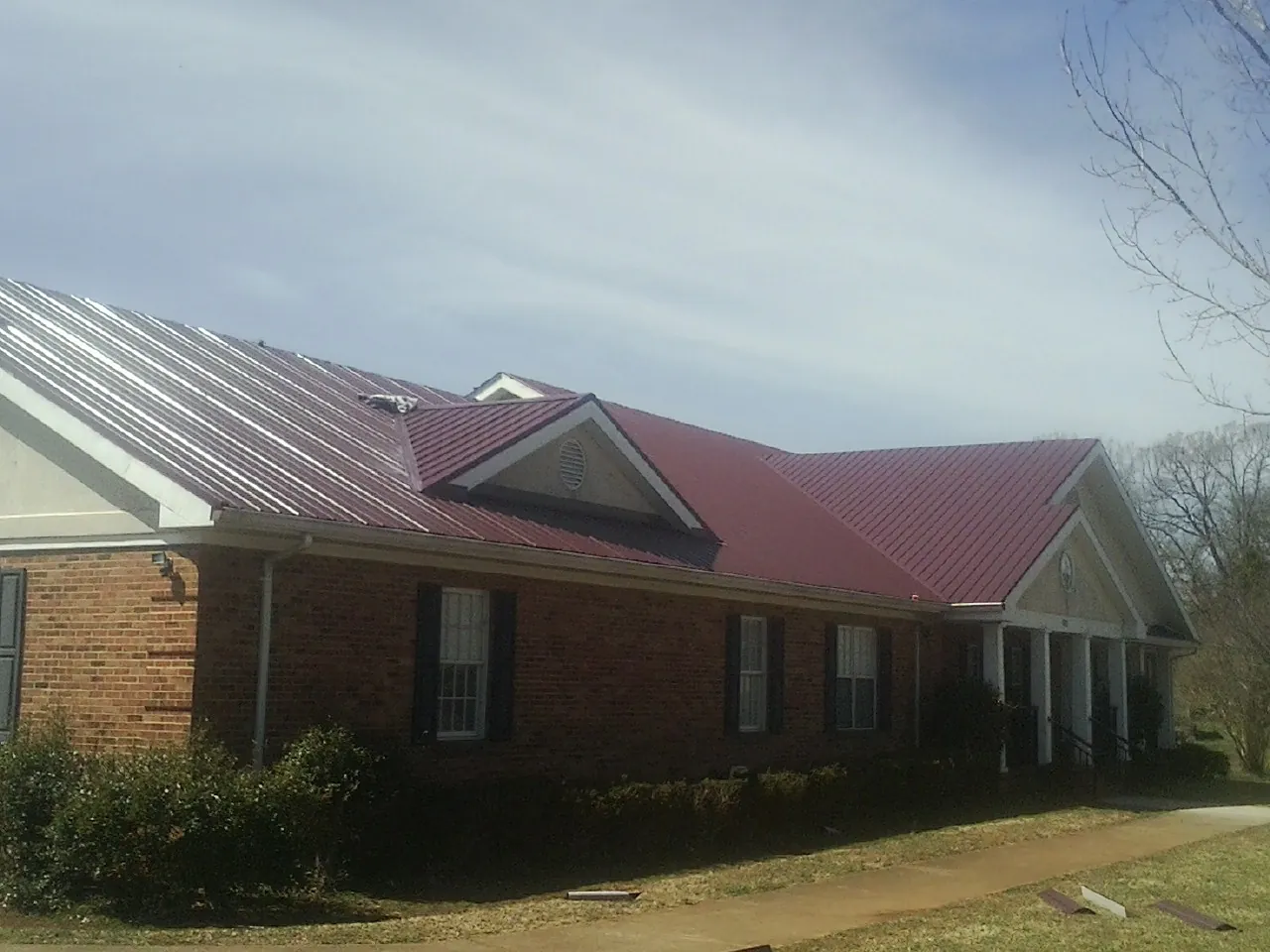 Red metal roof with gabled entries on a long brick building, from a Hail Damage Roof Repair job in Bronx