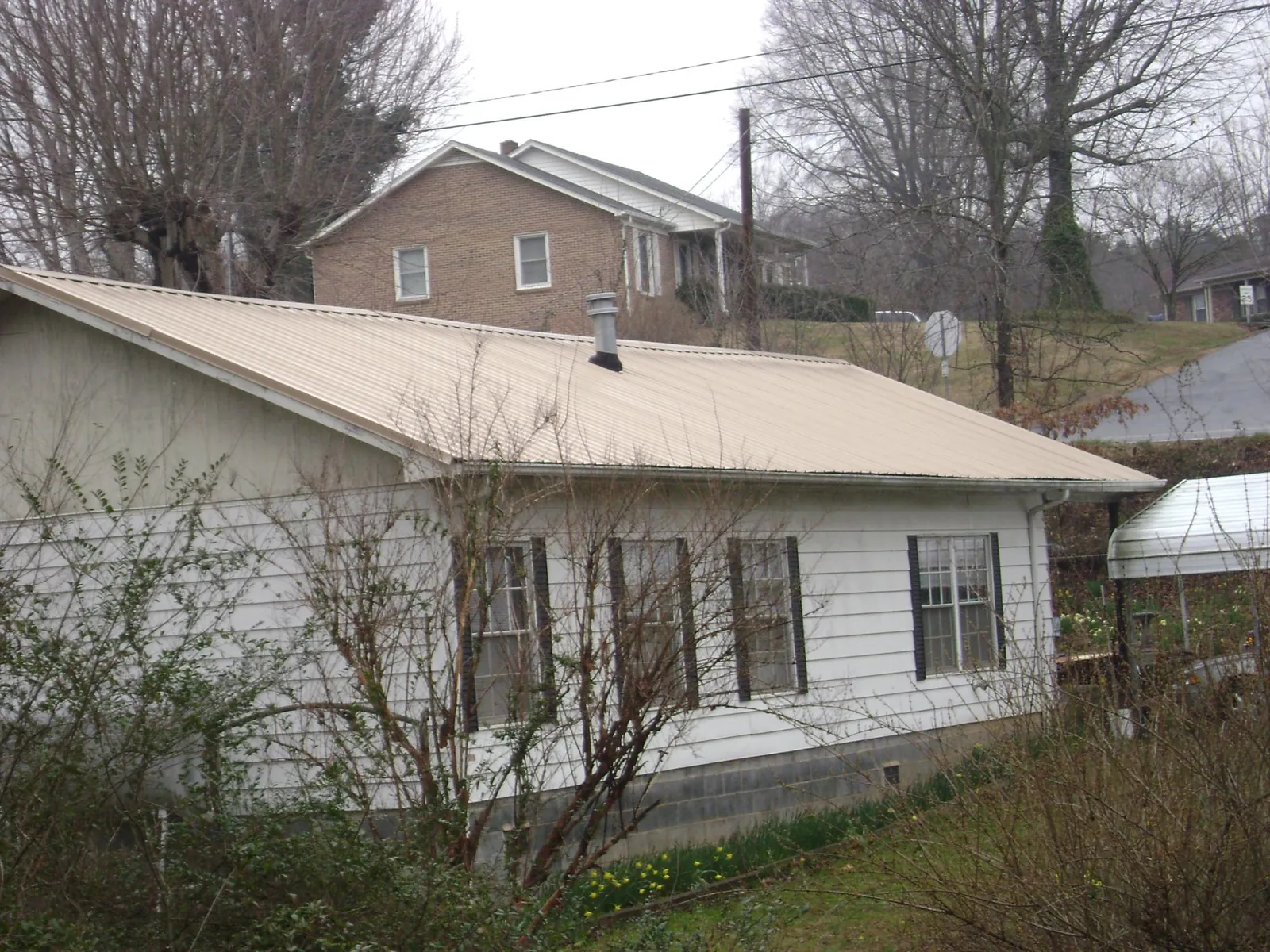 Tan metal roof on a white sided house set into a hillside — Commercial Roofing by Roofing Brothers in Bronx