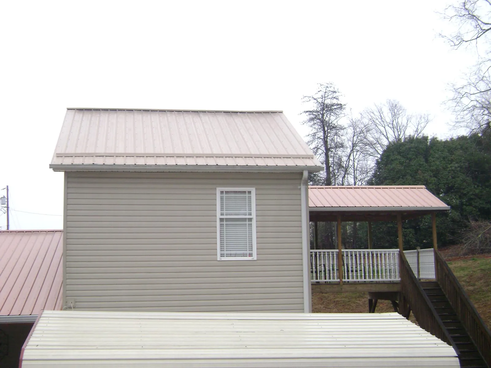 Tan metal roofs on a two story addition and attached porch, from a Roof Replacement job in Bronx